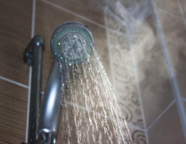 Low angle view of flowing shower head in the bathroom. Horizo<em></em>ntal composition. Image taken indoors and developed from Raw format. Focus on water. Shower head and other background are blurred.